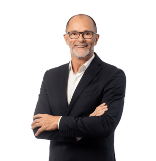 Mann im Anzug steht lächelnd mit verschränkten Armen.